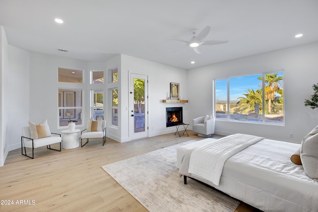 bedroom featuring light wood-style floors, access to outside, a lit fireplace, and recessed lighting