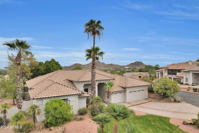 mediterranean / spanish-style home with concrete driveway, a tiled roof, an attached garage, a mountain view, and stucco siding