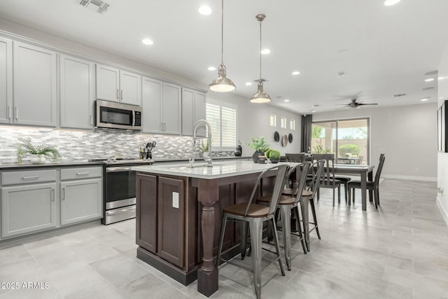 kitchen with visible vents, a kitchen island with sink, a sink, backsplash, and appliances with stainless steel finishes