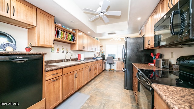 kitchen featuring ceiling fan, a raised ceiling, sink, black appliances, and dark stone counters