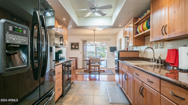 kitchen featuring a raised ceiling, sink, black appliances, ceiling fan with notable chandelier, and light hardwood / wood-style floors