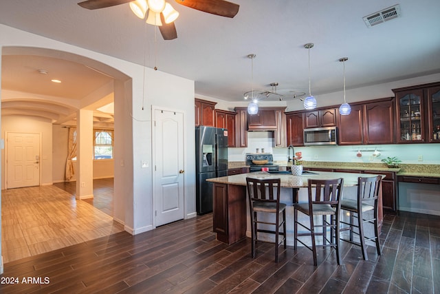 kitchen featuring appliances with stainless steel finishes, a kitchen island, decorative light fixtures, and dark hardwood / wood-style floors