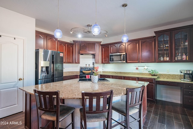 kitchen with dark hardwood / wood-style floors, stainless steel appliances, light stone countertops, a center island, and pendant lighting