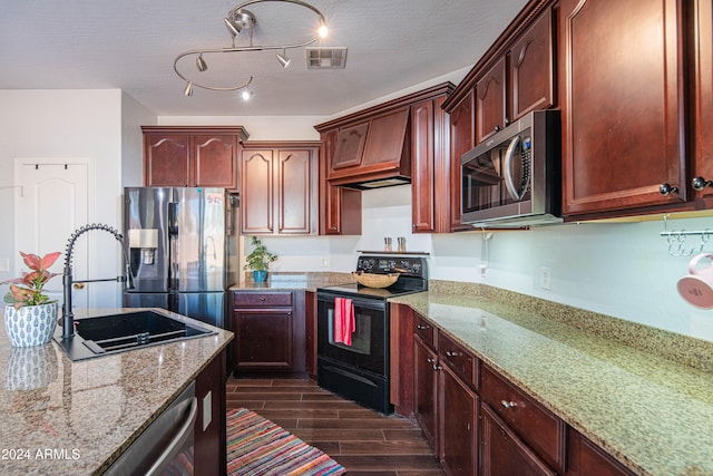 kitchen with sink, appliances with stainless steel finishes, light stone counters, a textured ceiling, and dark hardwood / wood-style flooring