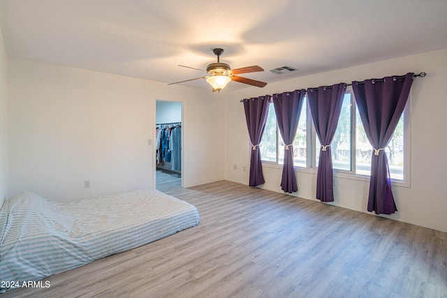 bedroom with a closet, ceiling fan, light hardwood / wood-style flooring, and a walk in closet