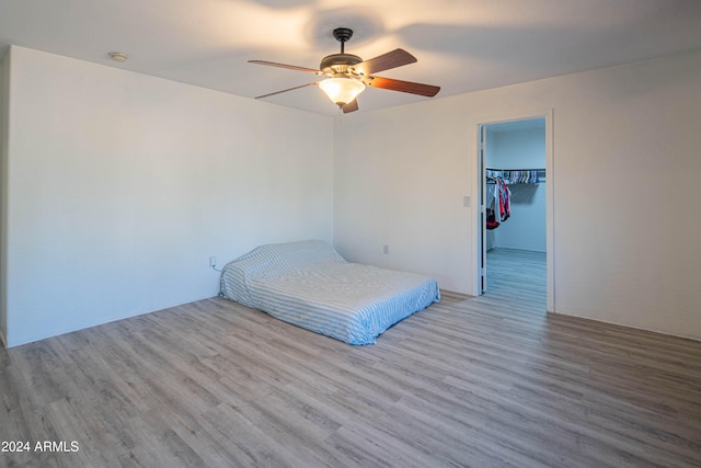 unfurnished bedroom with a closet, a walk in closet, light wood-type flooring, and ceiling fan