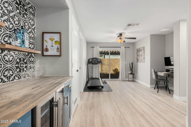 exercise room featuring light wood-type flooring, beverage cooler, and ceiling fan