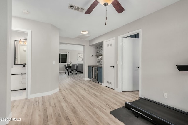 exercise room featuring ceiling fan, wine cooler, indoor bar, and light wood-type flooring