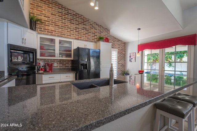 kitchen with black appliances, white cabinets, brick wall, and lofted ceiling