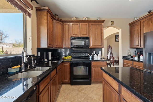 kitchen featuring sink, black appliances, light tile patterned floors, dark stone counters, and backsplash