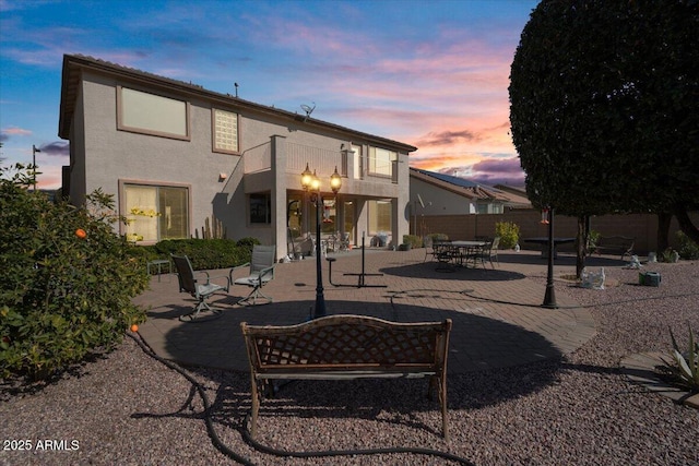 back house at dusk with a balcony and a patio area