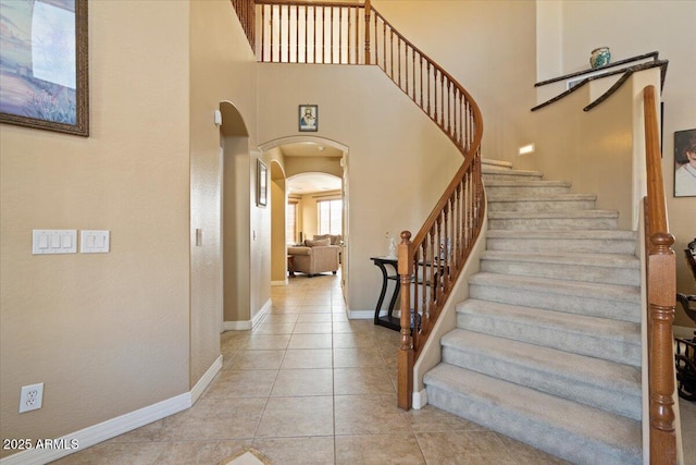 stairway with tile patterned floors and a high ceiling