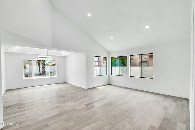 unfurnished living room with plenty of natural light, high vaulted ceiling, an inviting chandelier, and light wood-type flooring