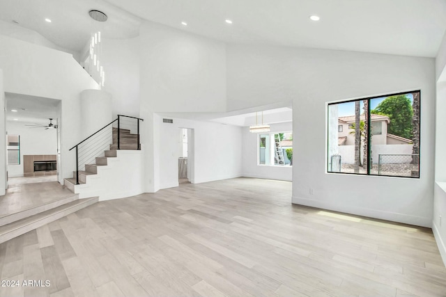 unfurnished living room with ceiling fan, high vaulted ceiling, and light hardwood / wood-style floors