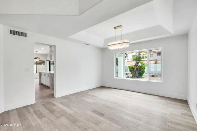 unfurnished room featuring a raised ceiling, an inviting chandelier, and light wood-type flooring