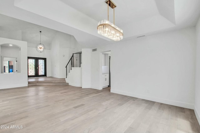 unfurnished living room featuring a chandelier, light hardwood / wood-style floors, a towering ceiling, and french doors