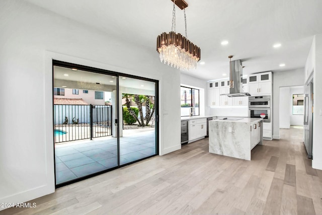 kitchen featuring island exhaust hood, decorative light fixtures, white cabinets, a center island, and light hardwood / wood-style floors