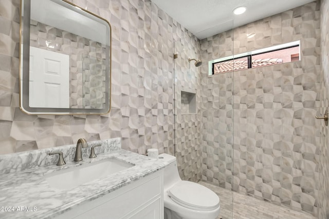 bathroom with toilet, vanity, tile walls, and tiled shower