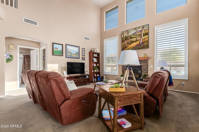 living room with light carpet, a towering ceiling, and a stone fireplace