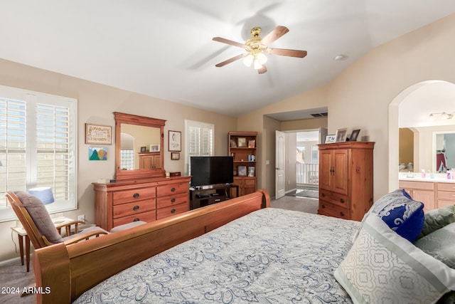 bedroom with ceiling fan, vaulted ceiling, multiple windows, and ensuite bath