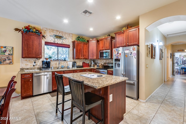 kitchen featuring a kitchen island, light stone countertops, stainless steel appliances, light tile patterned flooring, and a kitchen bar