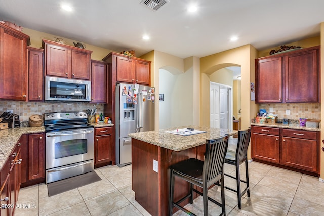 kitchen featuring tasteful backsplash, a kitchen island, stainless steel appliances, light stone countertops, and a kitchen bar