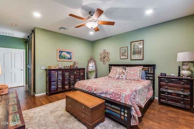 bedroom with a barn door, dark hardwood / wood-style floors, and ceiling fan