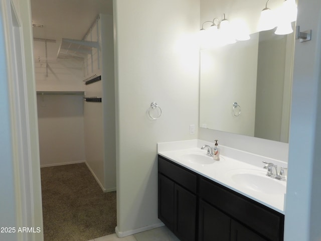 bathroom featuring double vanity, a spacious closet, baseboards, and a sink