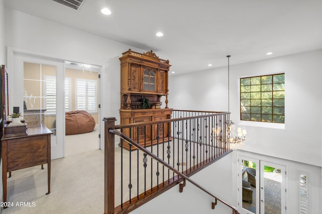 hall with a wealth of natural light, light colored carpet, and a notable chandelier