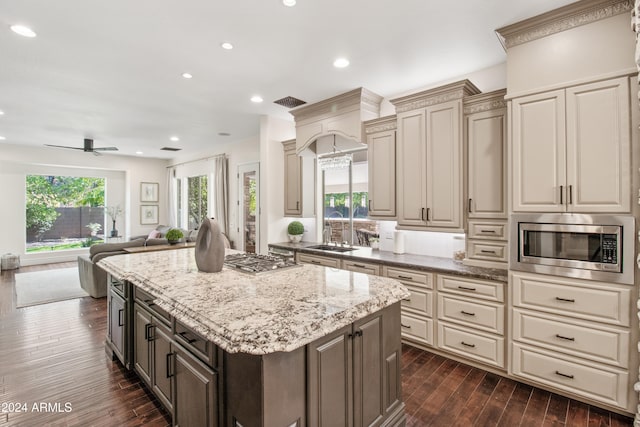 kitchen with appliances with stainless steel finishes, dark hardwood / wood-style flooring, ceiling fan, cream cabinetry, and a kitchen island