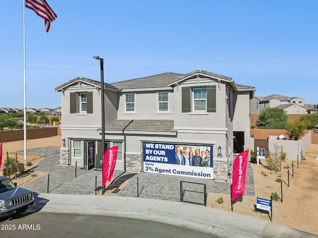 view of front facade with a tile roof, fence, stone siding, and stucco siding