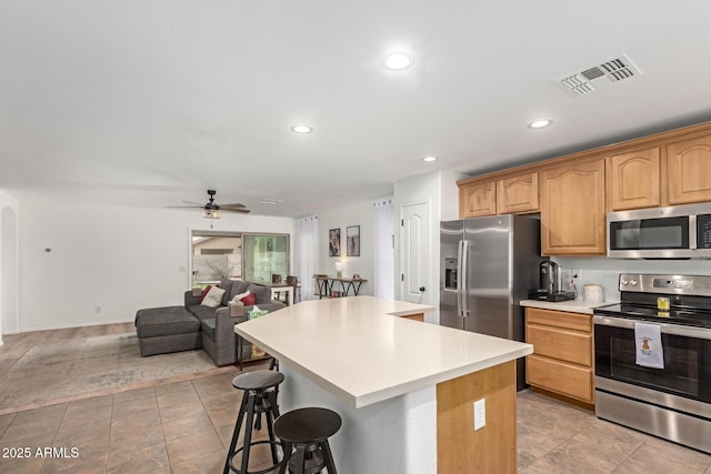 kitchen featuring a breakfast bar, a center island, light tile patterned floors, ceiling fan, and stainless steel appliances