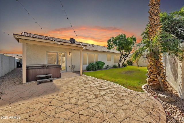 back house at dusk featuring a hot tub, a yard, and a patio area