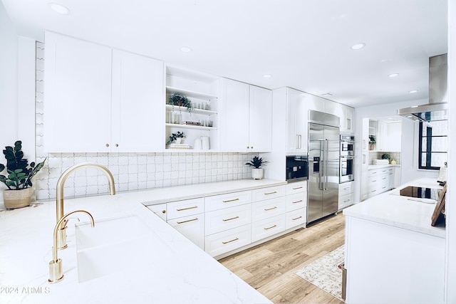 kitchen with stainless steel appliances, light stone counters, island exhaust hood, light hardwood / wood-style floors, and white cabinets