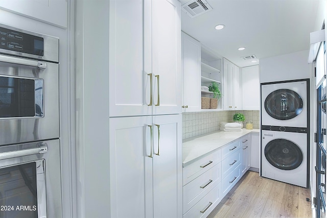 laundry area featuring a healthy amount of sunlight, stacked washer and clothes dryer, and light wood-type flooring