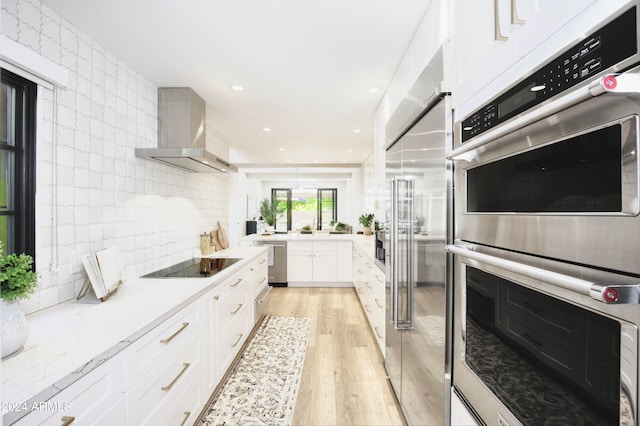 kitchen with white cabinets, light hardwood / wood-style floors, wall chimney range hood, and appliances with stainless steel finishes