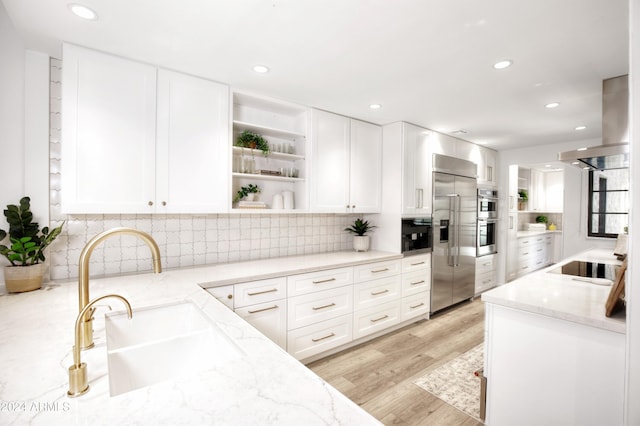 kitchen featuring island exhaust hood, stainless steel appliances, light stone counters, and white cabinetry