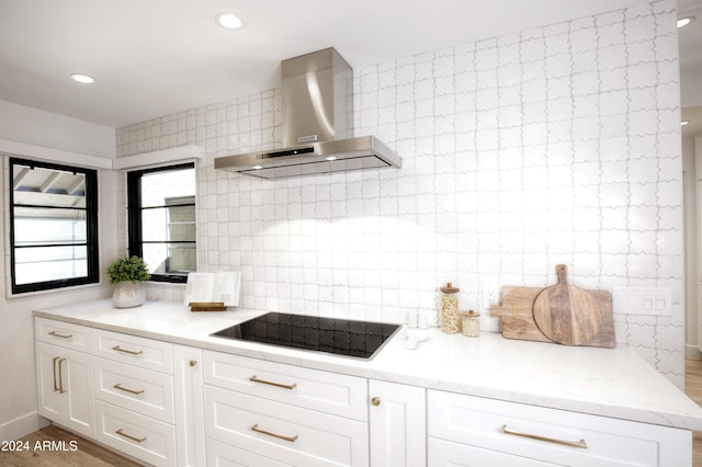 kitchen featuring light stone countertops, black electric stovetop, wall chimney exhaust hood, light hardwood / wood-style flooring, and white cabinets