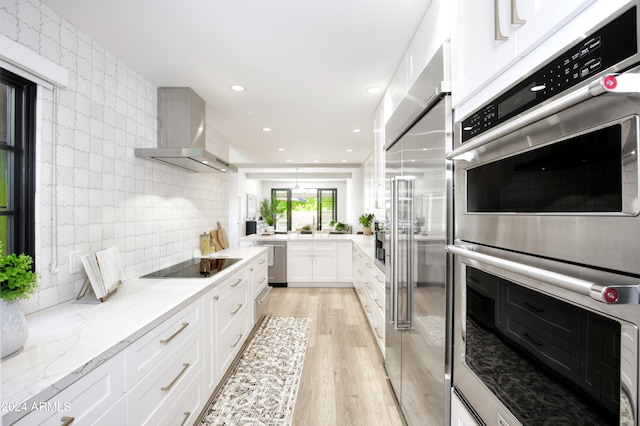 kitchen with light hardwood / wood-style flooring, wall chimney exhaust hood, light stone countertops, white cabinetry, and stainless steel appliances