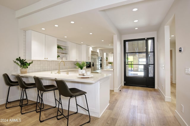 kitchen featuring kitchen peninsula, a kitchen bar, tasteful backsplash, light hardwood / wood-style flooring, and white cabinetry