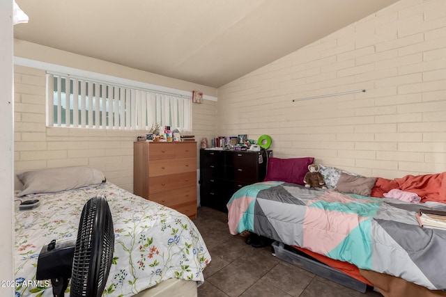 bedroom with dark tile patterned floors, brick wall, and vaulted ceiling