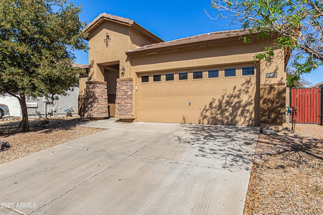 view of front facade with stucco siding, a gate, a garage, stone siding, and driveway