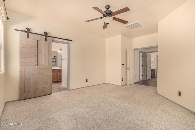 unfurnished bedroom with a barn door, connected bathroom, visible vents, baseboards, and carpet