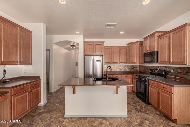 kitchen with dark countertops, visible vents, backsplash, a sink, and black appliances