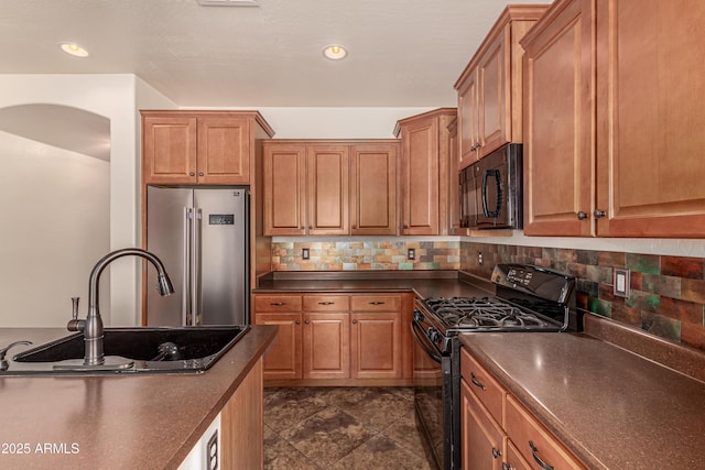 kitchen with tasteful backsplash, brown cabinetry, dark countertops, black appliances, and a sink