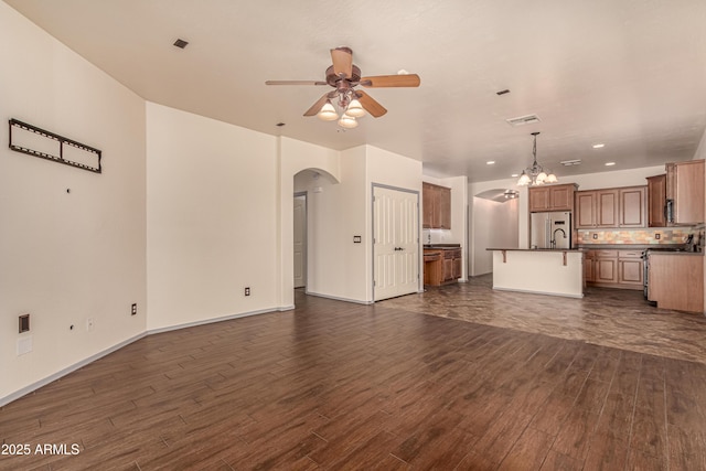 unfurnished living room featuring baseboards, visible vents, arched walkways, dark wood-type flooring, and ceiling fan with notable chandelier