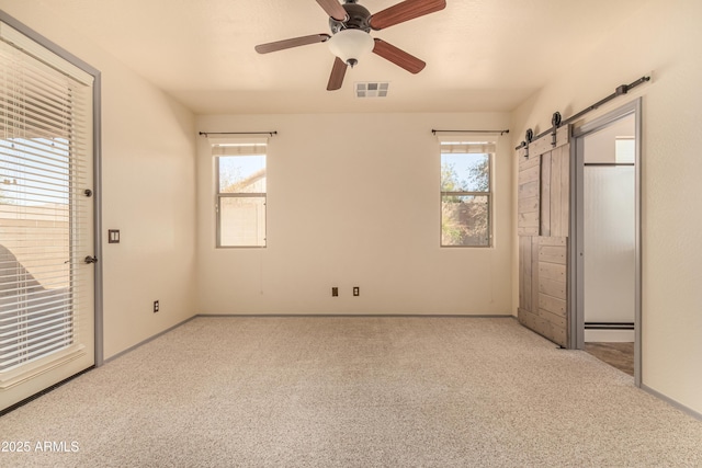 unfurnished bedroom with multiple windows, visible vents, carpet flooring, and a barn door