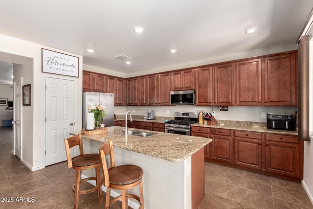 13123 W Cottontail Ln, Peoria, AZ 85383 - kitchen featuring appliances with stainless steel finishes, a sink, a kitchen island with sink, light stone counters, and a kitchen bar