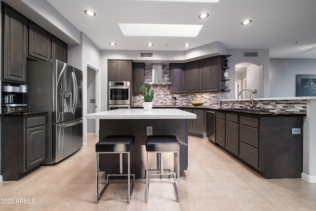 kitchen with a breakfast bar area, appliances with stainless steel finishes, backsplash, dark brown cabinets, and a kitchen island