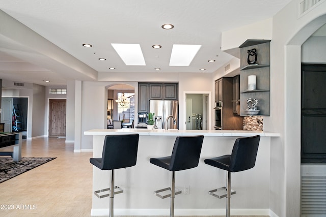 kitchen featuring a kitchen breakfast bar, kitchen peninsula, gray cabinets, stainless steel appliances, and backsplash